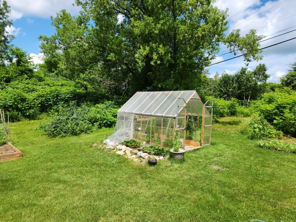 Picture of greenhouse with garden bed along side of it.