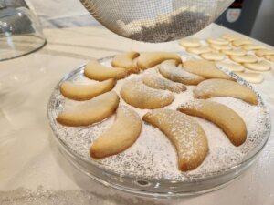 Sifting powdered sugar ontop of spread out greek christmas cookies