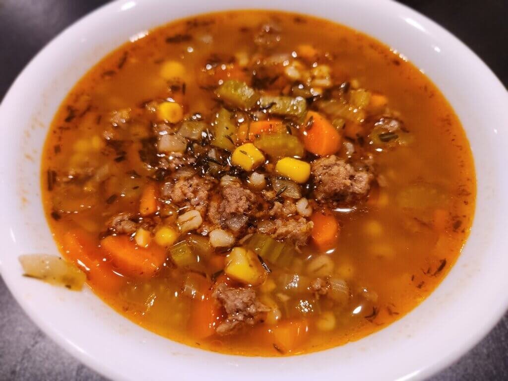 Bowl of homemade beef and barley soup with ground beef, carrots, celery, corn, and pearl barley