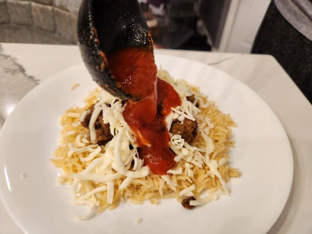 Pouring tomato sauce over lentil meatballs and rice