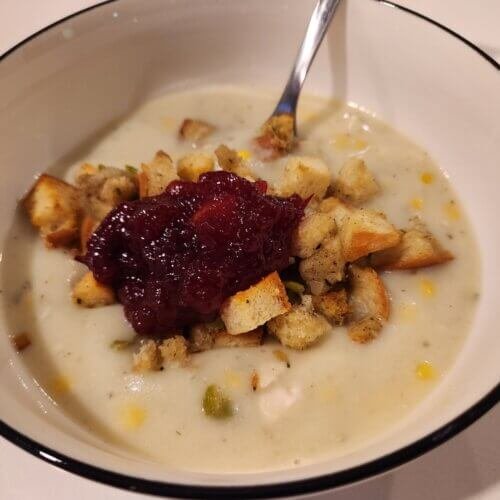 Creamy chicken chowder topped with stuffing croutons and cranberry sauce in a white bowl