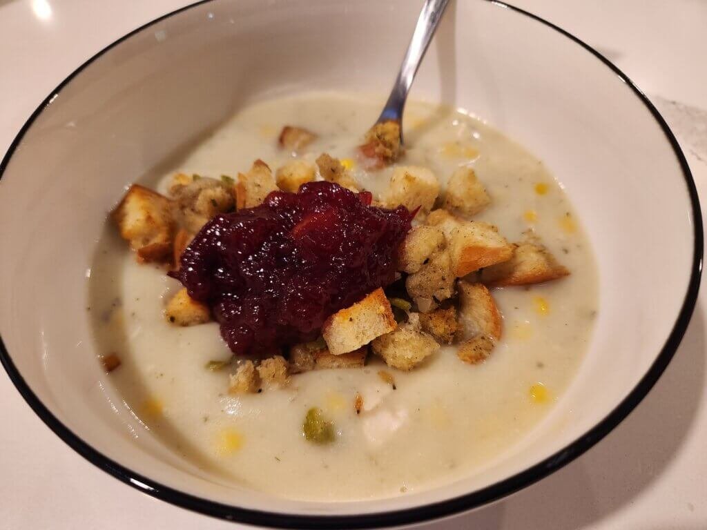Creamy chicken chowder in a serving bowl topped with stuffing croutons and cranberry sauce