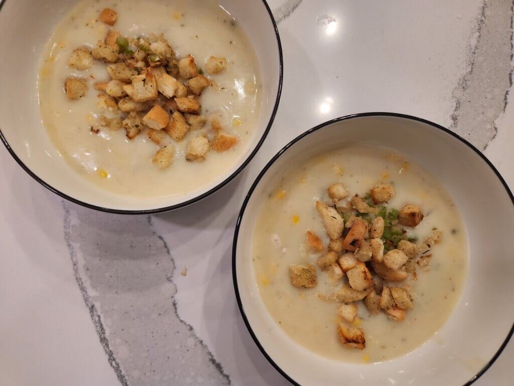 Two bowls of creamy chicken chowder with stuffing croutons on top.