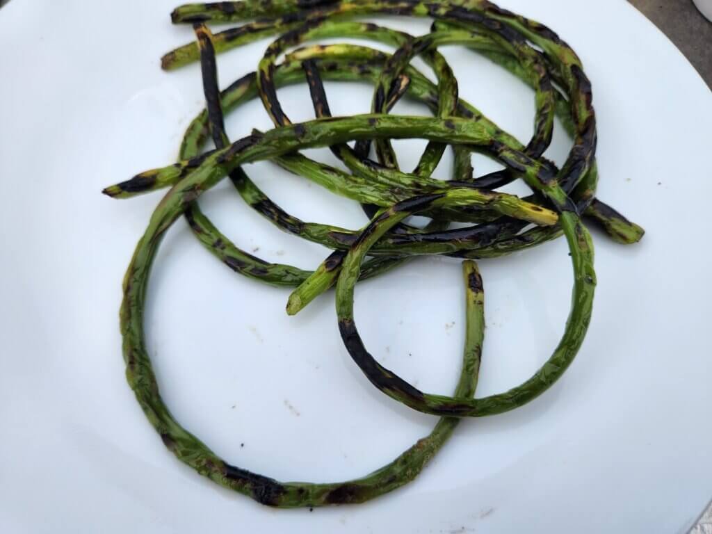 Garlic scapes grilled until lightly charred and served on a white plate