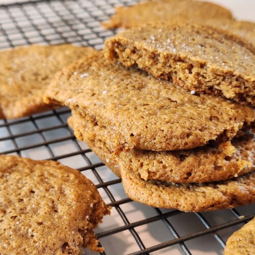 Homemade pumpkin spice cookies stacked on a cooling rack with one broken open to show the soft center.