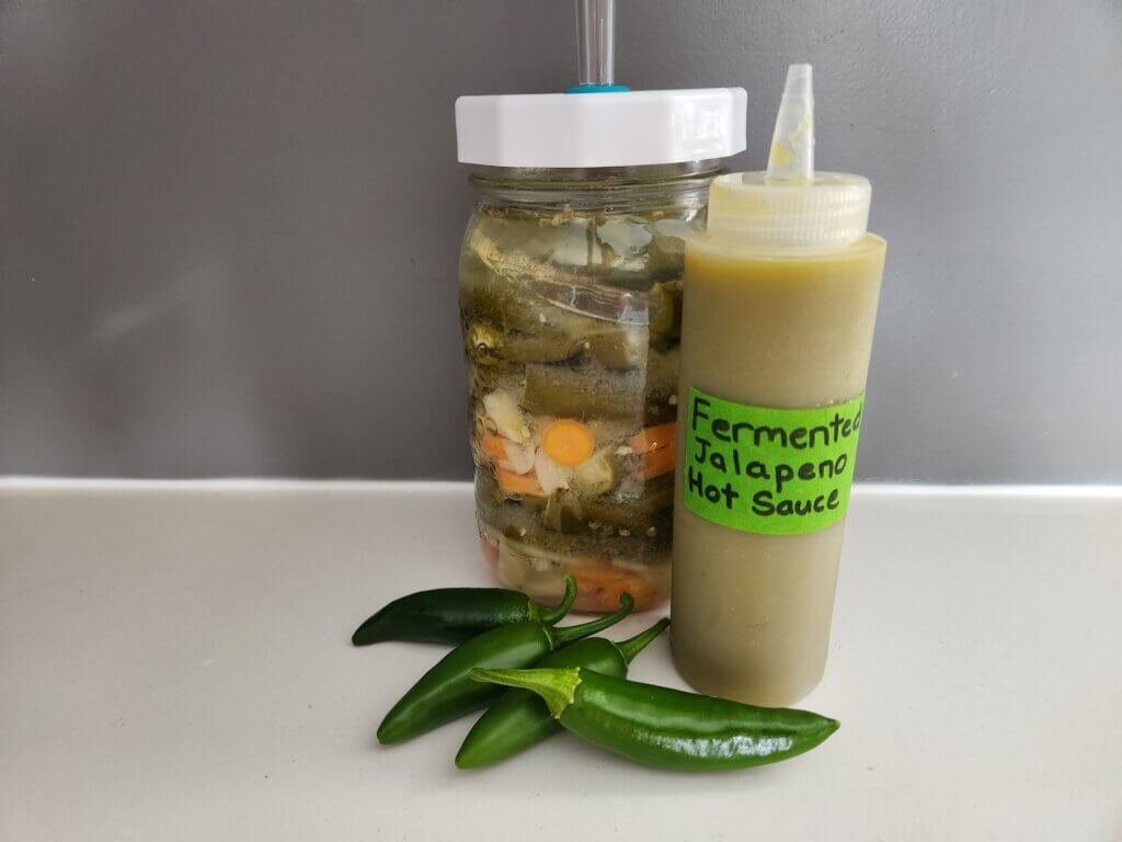 Homemade fermented jalapeño hot sauce with fresh jalapeños and a fermentation jar