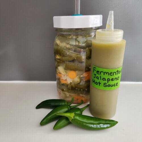 Homemade fermented jalapeño hot sauce with fresh jalapeños and a fermentation jar