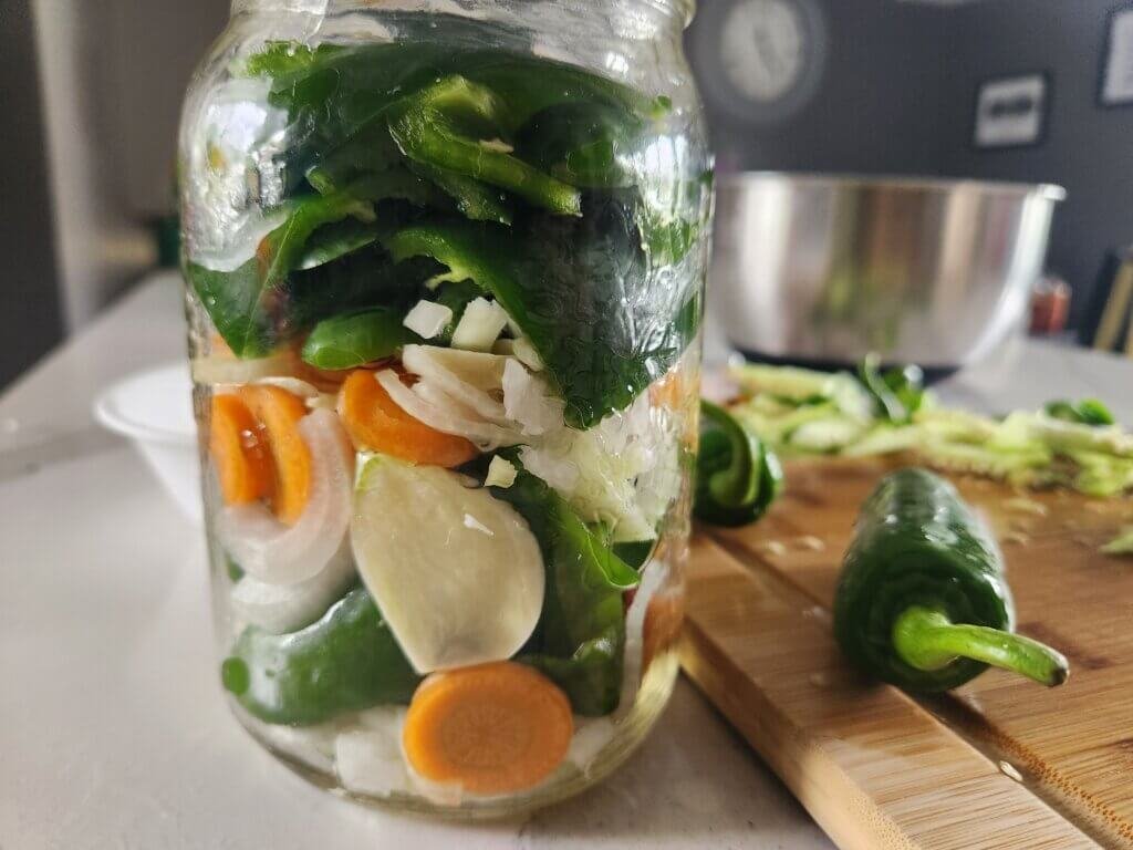 Packing jalapeños, carrots, onion and garlic into a jar for fermented hot sauce