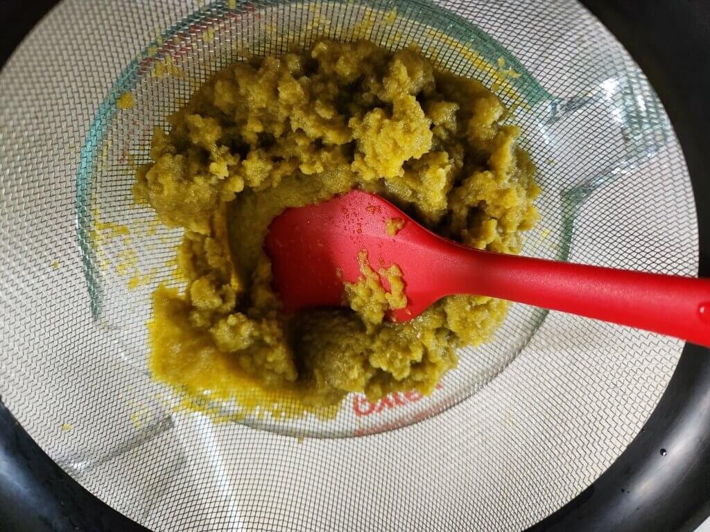 Straining blended fermented jalapeño hot sauce through a fine mesh strainer