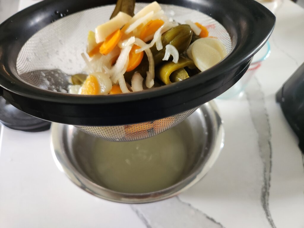 Straining fermented jalapeños, carrots, onion and garlic from the brine