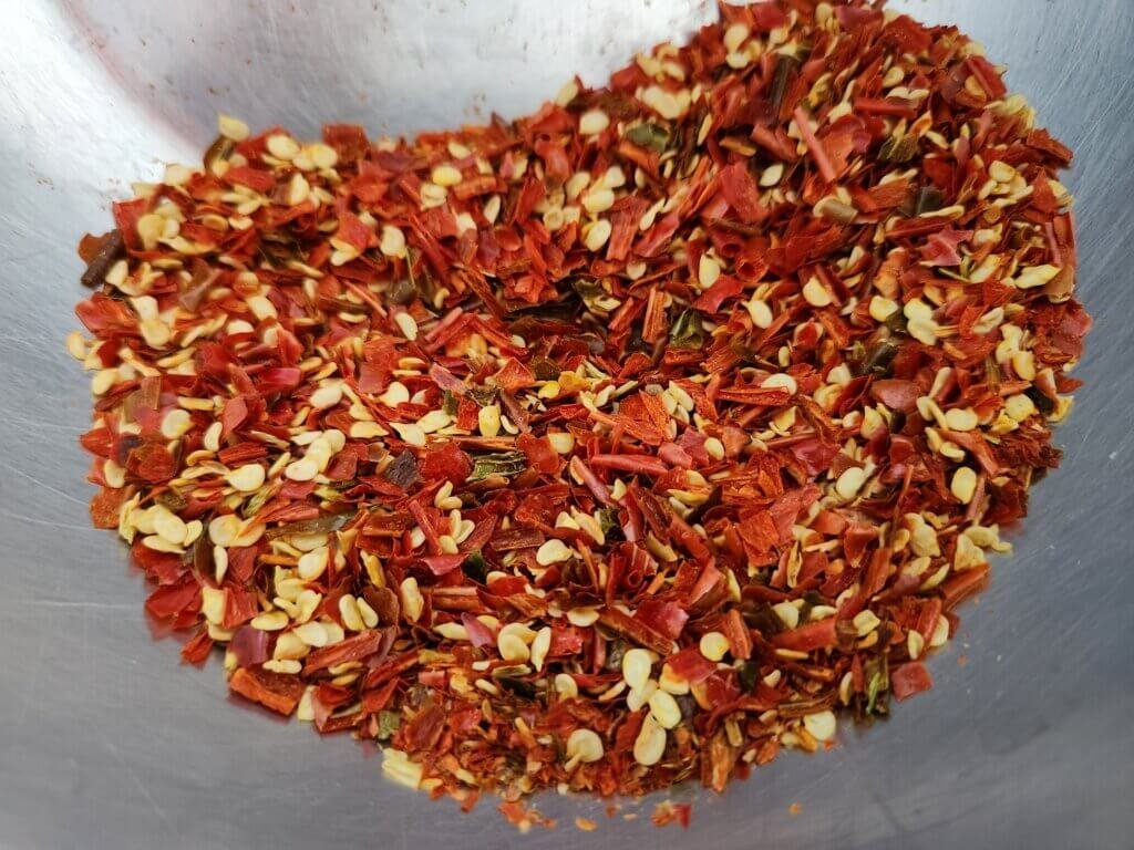 Homemade crushed red pepper flakes made from dehydrated cayenne peppers, showing red pepper pieces and yellow seeds.